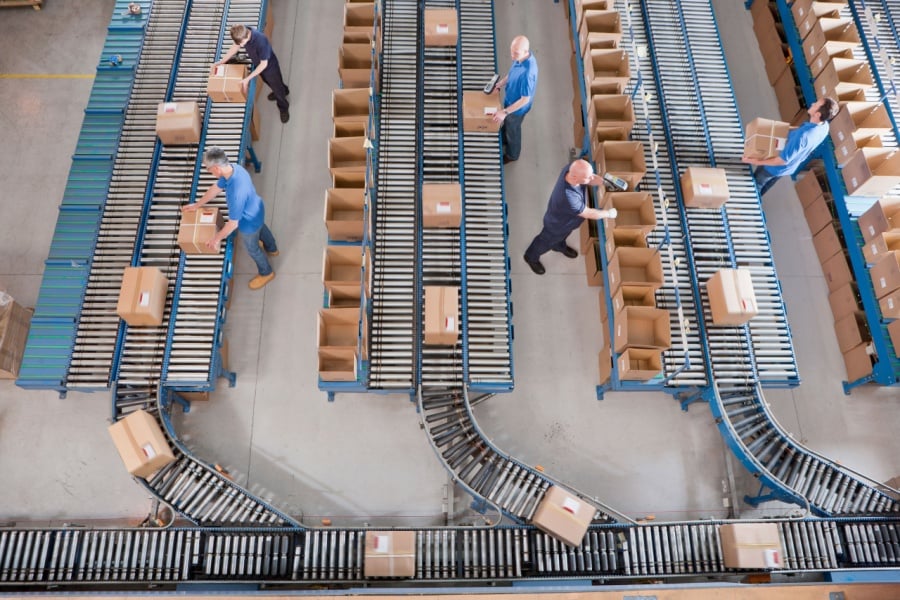 warehouse workers fulfilling orders as parcels roll on conveyance systems.